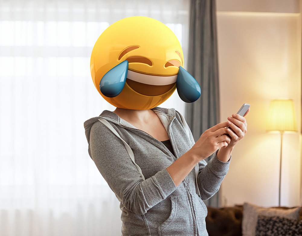 Na imagem, uma pessoa está com o emoji haha em seu rosto enquanto segura o smatphone, reagindo às várias situações que o marketing de conteúdo proporciona.